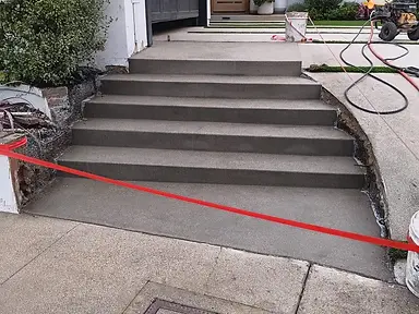 Freshly finished concrete entry steps and front walkway leading to a modern white home with a wood front door.