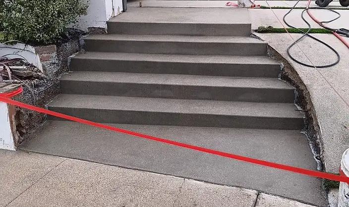 Freshly poured concrete entry steps and front walkway leading to a modern white home with a wood front door