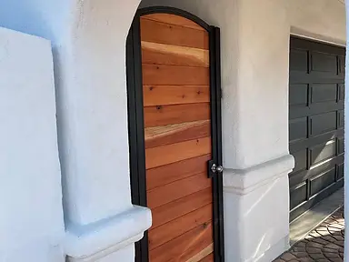 Arched cedar wood entry gate set in a black steel frame within a white stucco archway entrance