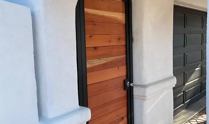 Arched cedar wood entry gate set in a black steel frame within a white stucco archway entrance