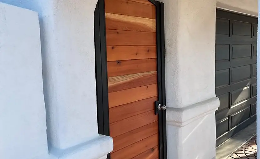 Arched cedar wood entry gate set in a black steel frame within a white stucco archway entrance