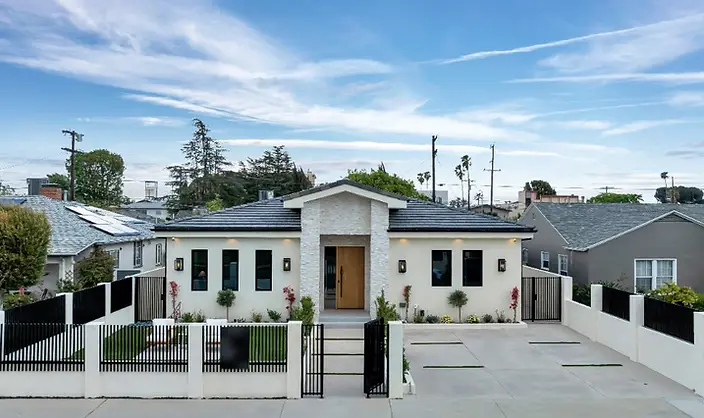 Full-width street view of Valley Glen new-construction home with cream stucco, stacked-stone entry, black iron fence, and concrete driveway.