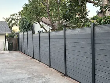 A completed gray composite privacy fence with black metal posts.
