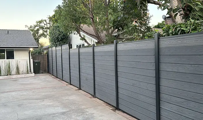 A completed gray composite privacy fence with black metal posts.