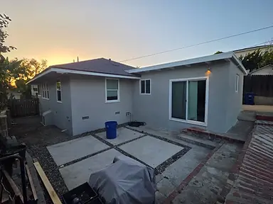 Backyard elevation of a warm-gray painted stucco home with white window trim and a sliding door at dusk.