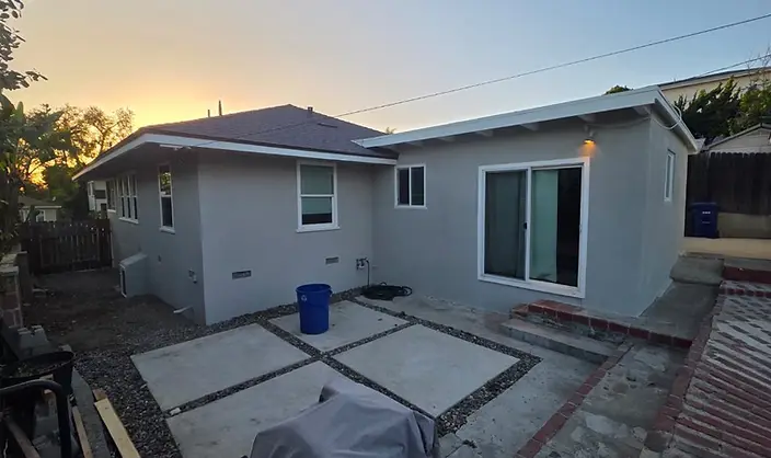 Backyard elevation of a gray painted stucco home with white window trim and sliding door at dusk