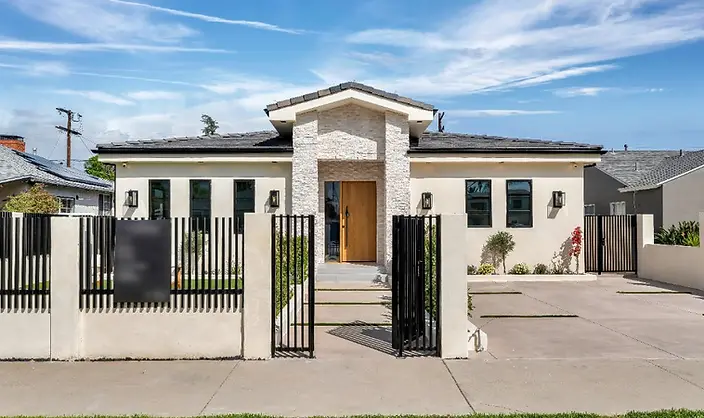 Close-up of new-construction Valley Glen home entry featuring stacked-stone tower, natural wood pivot door, black steel pedestrian gate, and concrete hardscape.