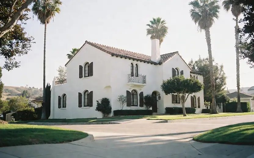 Two-story white Spanish Colonial stucco home with a tile roof and dark shutters after an exterior repaint.