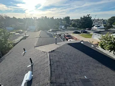 Completed charcoal architectural-shingle roof with finished ridge caps and roof penetrations.
