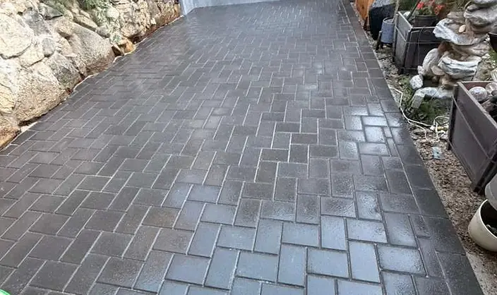 Charcoal grey concrete pavers laid in a herringbone pattern forming a side driveway between a stone retaining wall and a cedar fence