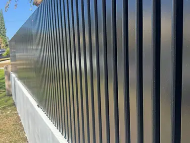 Perspective view of black metal fence slats mounted on a concrete wall.