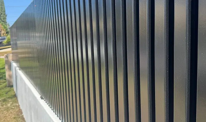 Perspective view of black metal fence slats mounted on a concrete wall.