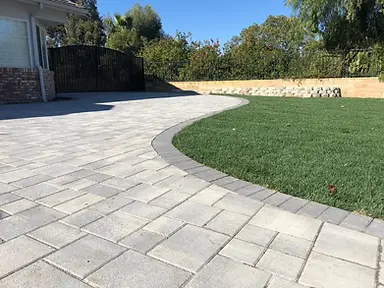 Tumbled concrete paver patio with a curved soldier-course border meeting a green lawn in a Los Angeles backyard