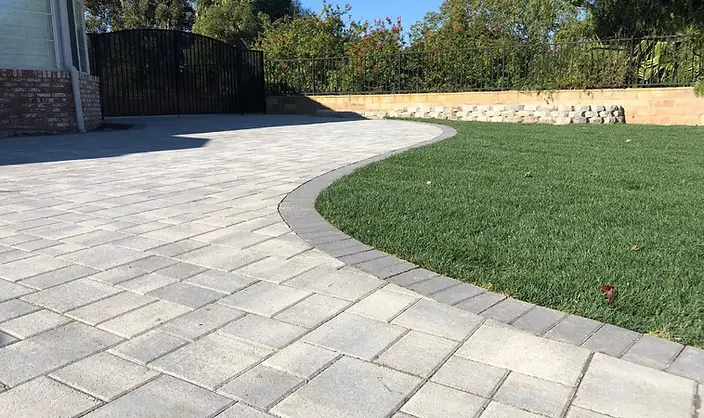 Tumbled concrete paver patio with a curved soldier-course border meeting a green lawn in a Los Angeles backyard