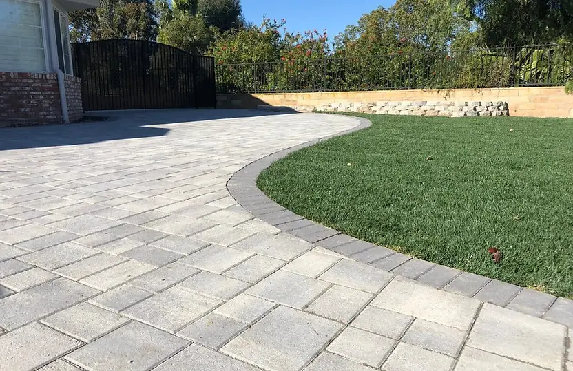 Completed curved concrete-paver patio with a darker soldier-course border meeting a green lawn in a residential backyard.