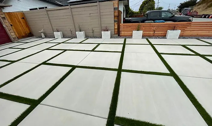 Large-format white concrete paver courtyard with artificial turf joints beside a horizontal cedar fence