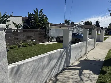 Finished white stucco front yard wall with square pillars and gravel border along a sidewalk