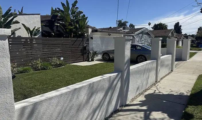 Finished white stucco front yard wall with square pillars and gravel border along a sidewalk