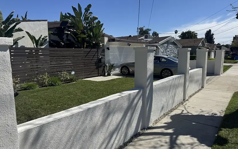Completed white stucco front-yard wall with square pillars and a gravel border along the sidewalk.