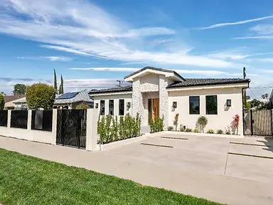 Angled street view of new-construction Valley Glen home with cream stucco, stacked-stone entry tower, black steel privacy fence, solar panels, and concrete driveway.