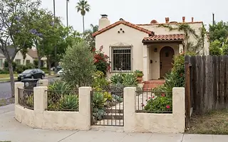 Editorial illustration: Low front-yard fence at the sidewalk of a Spanish-style Los Angeles bungalow with a taller side-yard fence behind the gate