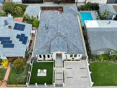 Drone aerial view of a completed new-construction home in Valley Glen, showing the concrete driveway, synthetic turf front yard, steel fence, and shingle roof.