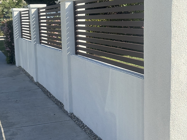 Completed white stucco perimeter wall with dark horizontal metal slat panels between square pillars.