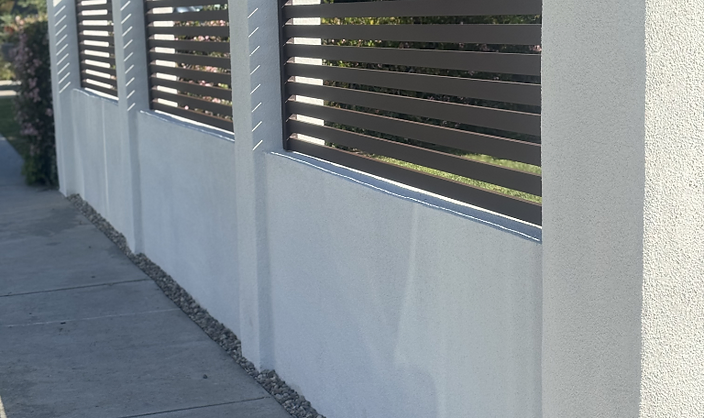 White stucco perimeter wall topped with dark horizontal metal slat panels between pillars