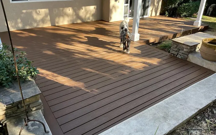 Completed brown composite deck extending from the house to a covered patio, with a clean picture-frame border and step transition.