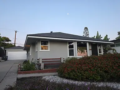 A grey stucco house with a dark shingle roof and garden landscaping.