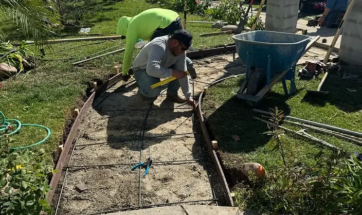Crew setting curved wood forms and rebar for a new concrete front walkway across a front lawn