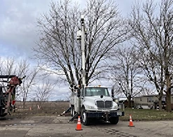 White bucket truck and grapple truck staged on a job site