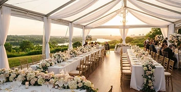 Elegant white frame tent at a wedding reception with floral table settings and gold chairs during golden hour