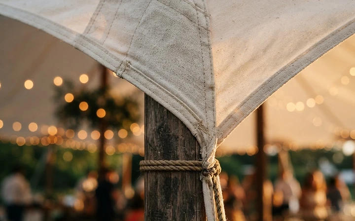 Close-up of premium white sailcloth tent fabric with warm fairy light bokeh at golden hour