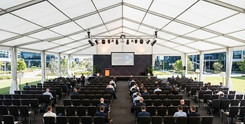 Large commercial tent set up for a corporate event with rows of chairs and professional lighting