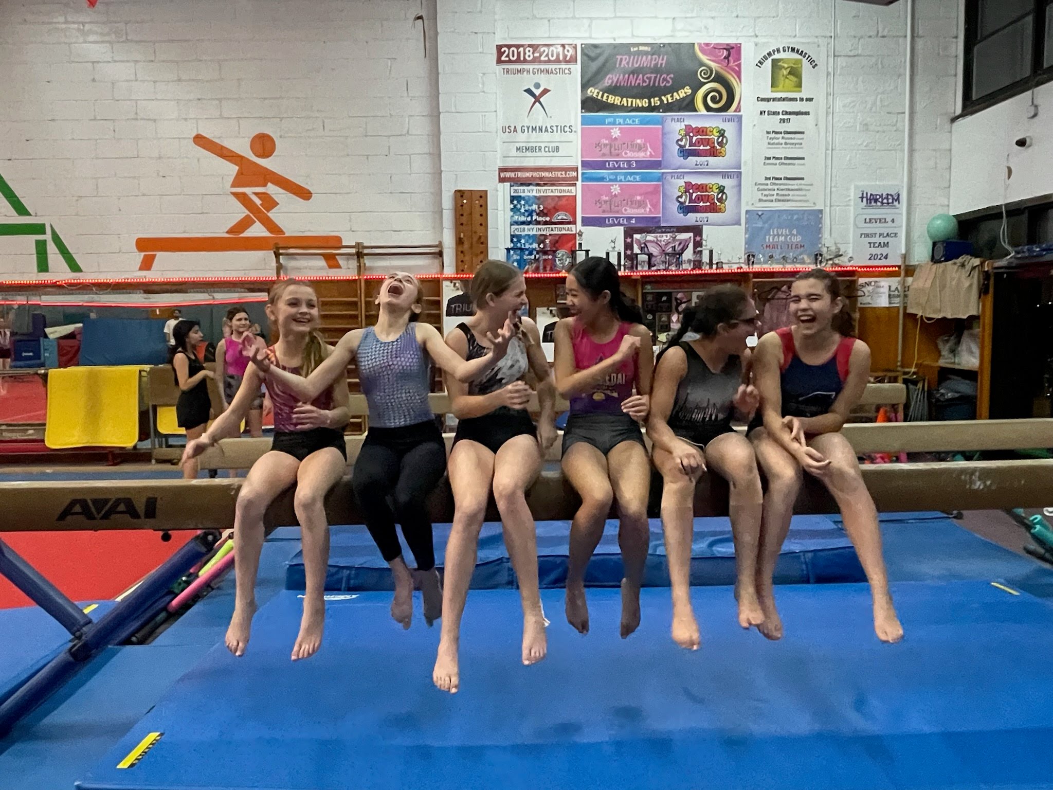 Gymnasts laughing together on the balance beam at Triumph Gymnastics