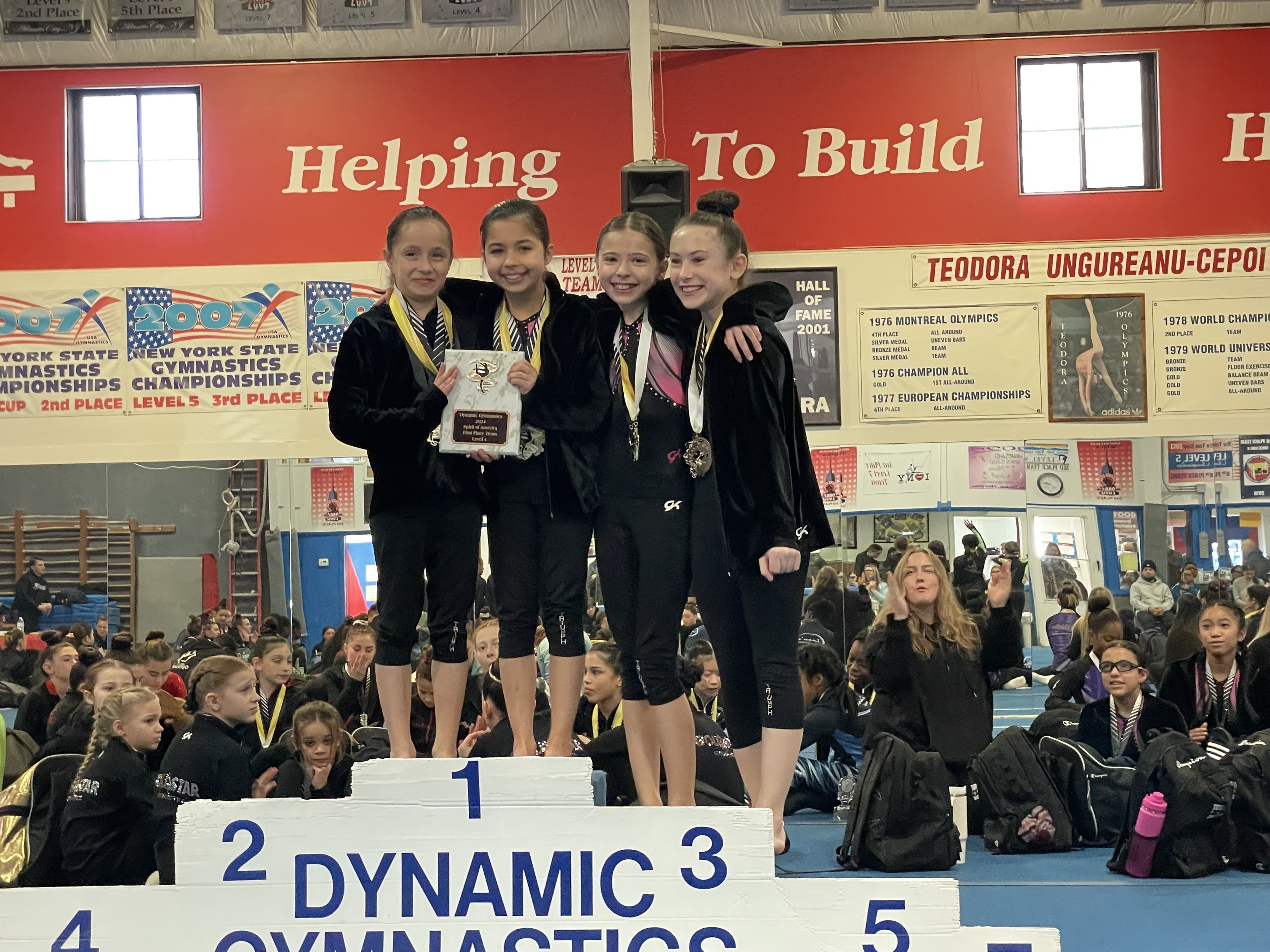Triumph Gymnastics team gymnasts on the podium with medals and a team trophy
