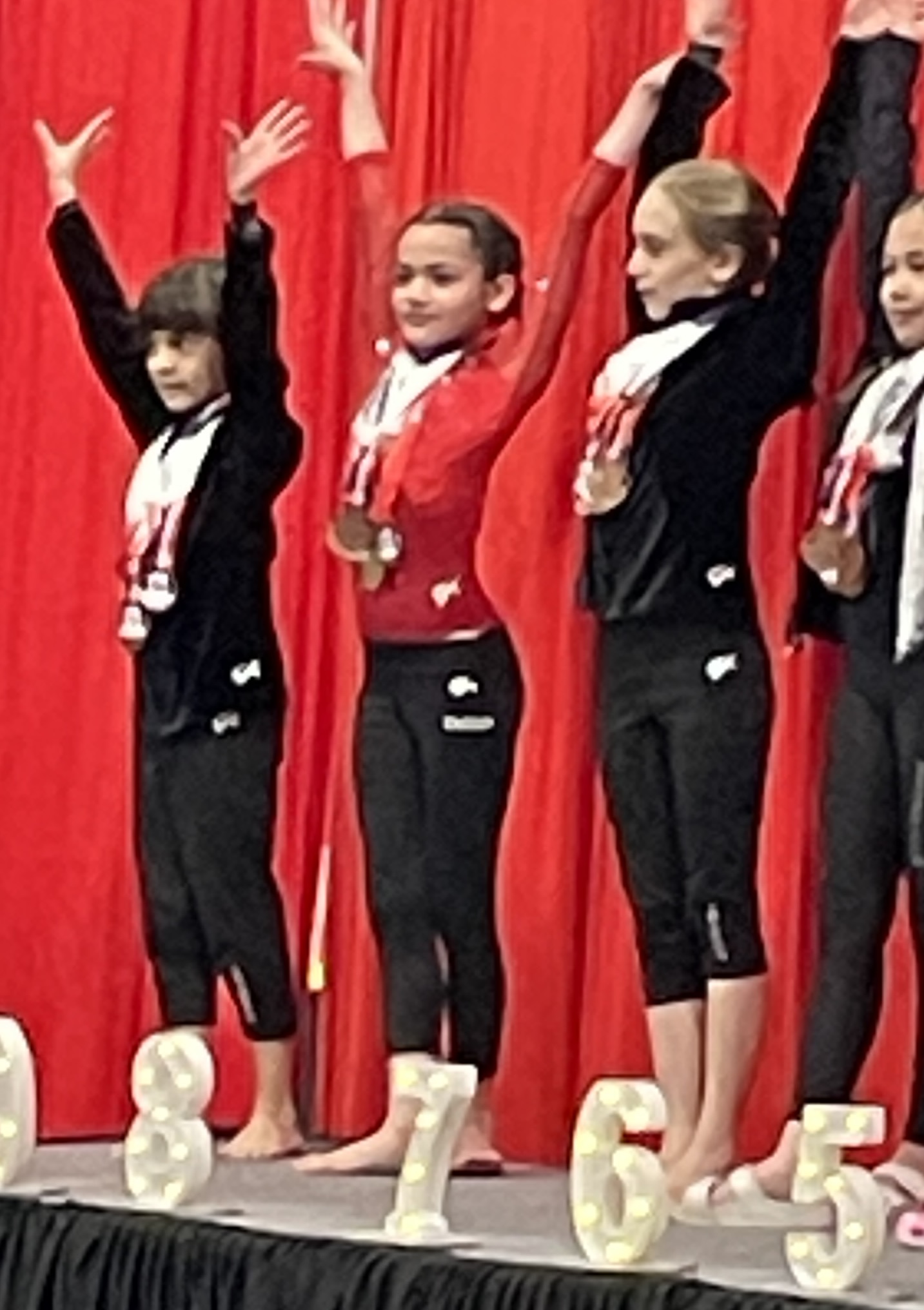 Young gymnasts with medals standing on awards stage with red curtain backdrop