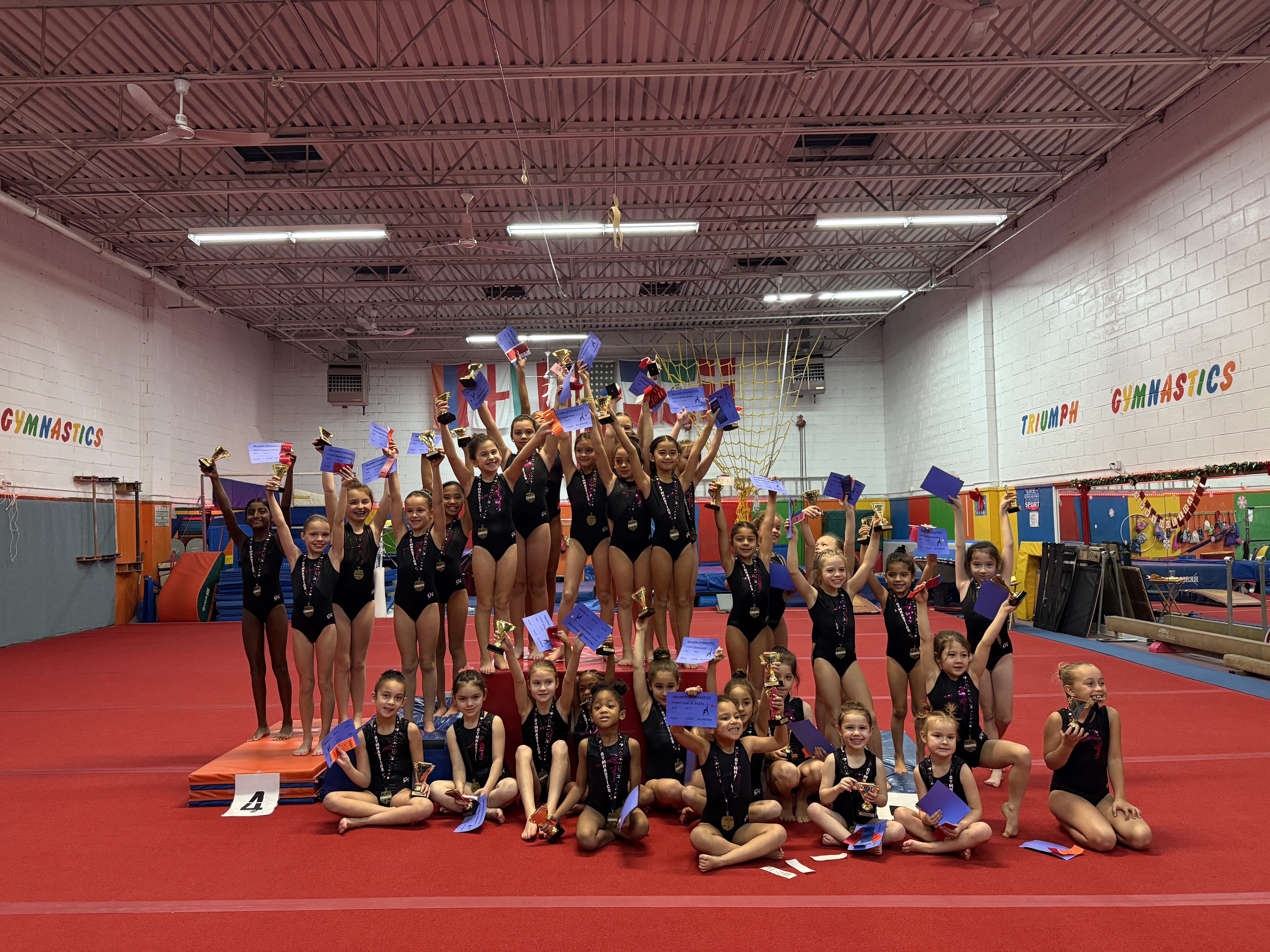 Triumph Gymnastics team gymnasts posing with their trophies and award ribbons after a competition