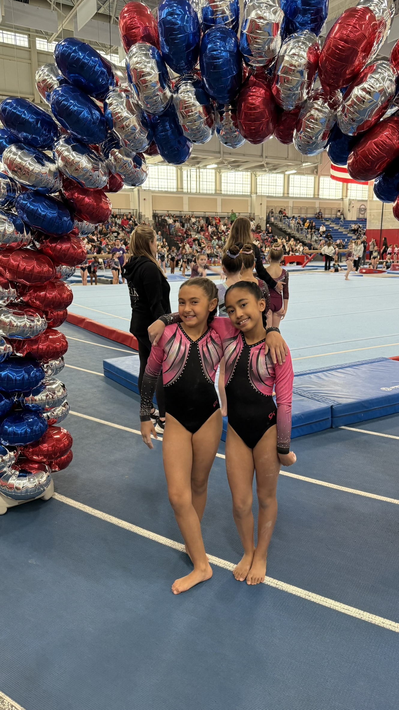 Two Triumph Gymnastics teammates smiling and hugging at a celebration
