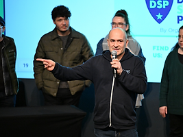 Billy Wimsett speaking and gesturing at a RootsCamp event panel.