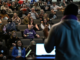 A packed RootsCamp auditorium during a keynote, viewed from behind the speaker's podium.