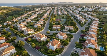 Vista aérea de um bairro residencial português com casas brancas e jardins ao final do dia