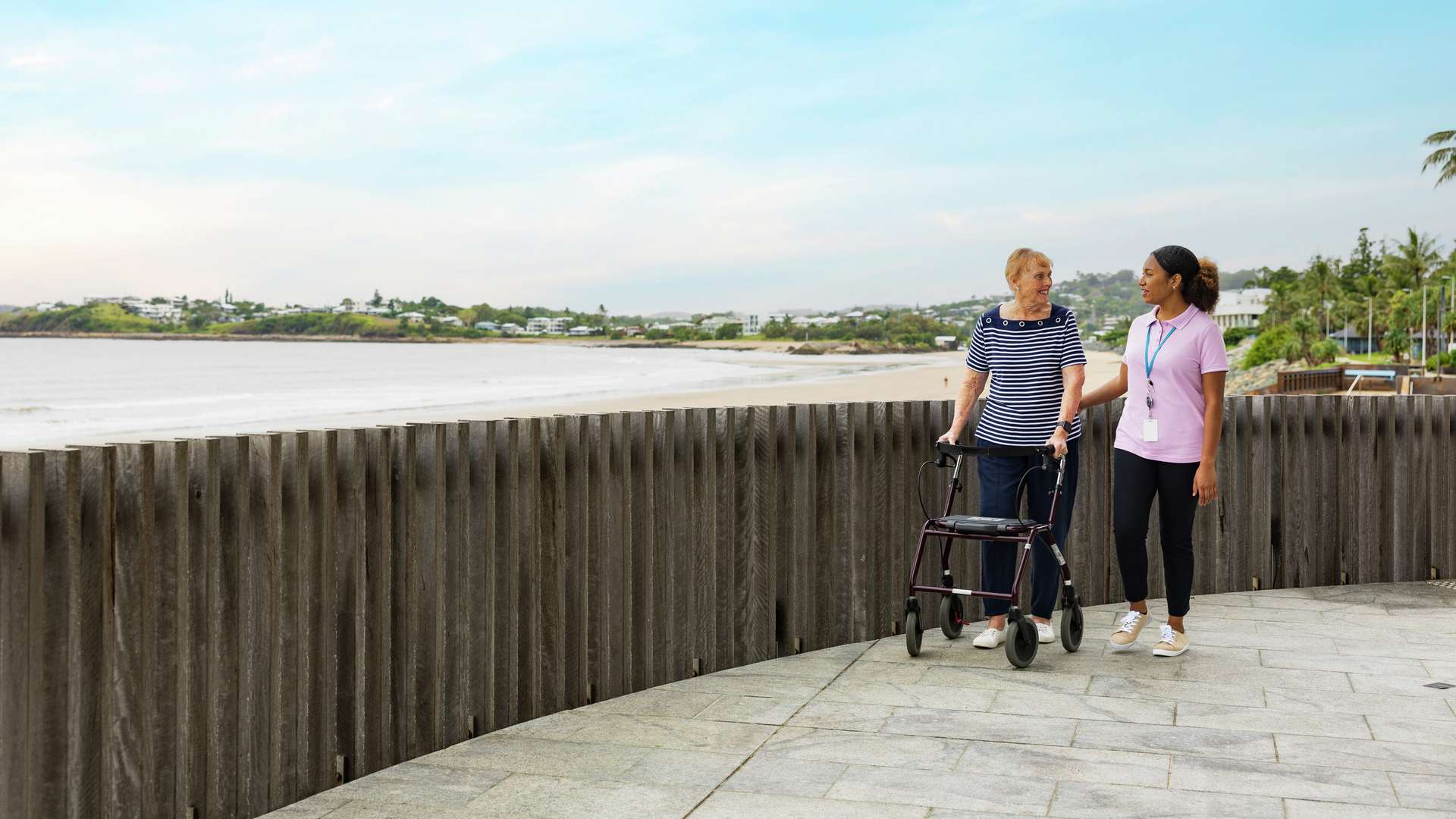 Support worker walking with an older woman along a coastal promenade