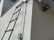 Exterior dome camera and LED floodlight mounted on a rendered wall, accessed by telescopic ladder