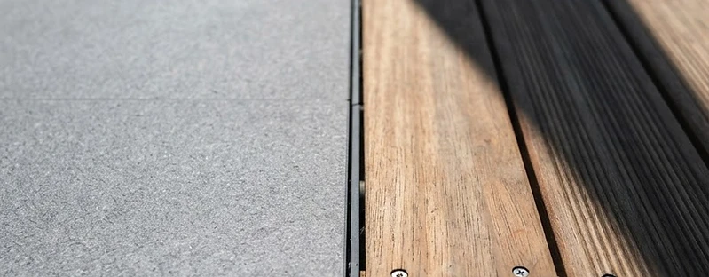 Macro detail of matte grey porcelain paving meeting warm teak decking with a precise joint