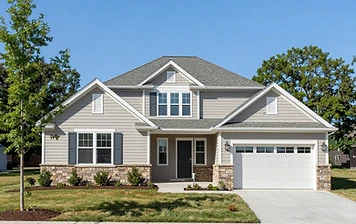 Two-story Chantilly, VA suburban home with light-gray vinyl siding, a stone-veneer foundation, a dark gray asphalt shingle roof with multiple gables, and a two-car garage under a clear blue sky