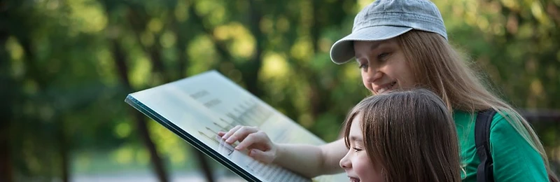 A mother and daughter looking at an exhibit sign together on a nature trail