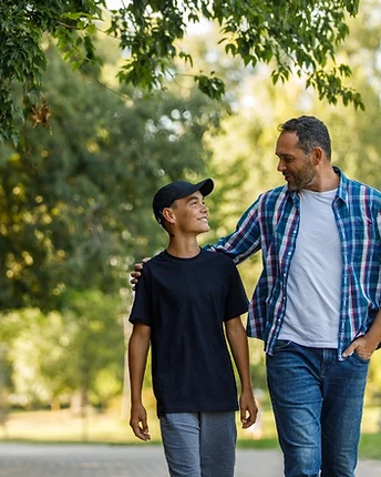 A father with his arm around his teenage son, walking together along a park path