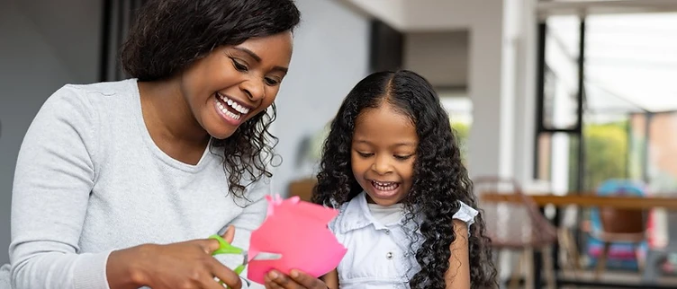 A woman and a young girl laughing together while cutting colorful construction paper at a table